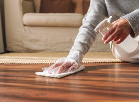Closeup image of a woman wearing protective glove, cleaning and washing wooden floor at home