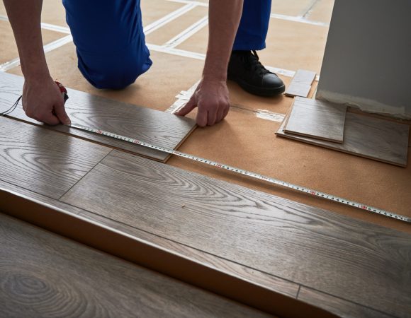 Close up of man construction worker checking distance from wall to laminate board. Male builder using tape measure while installing laminate flooring in apartment under renovation.